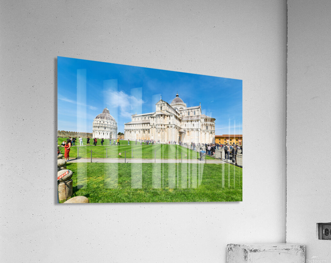 People walk in Piazza dei Miracoli admiring the Baptistry and Cathedral in Pisa. The sun shines on the historic buildings and green grass. Acrylic Print