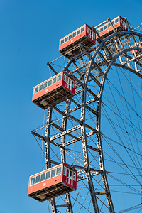 Ferris wheels red cabins against a clear blue sky.