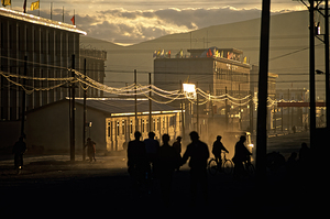 People walk and ride bikes along a dusty street at sunset in Tib