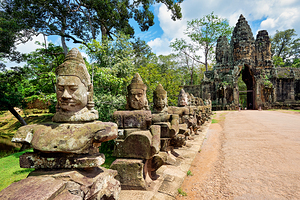 Ancient stone statues line path to Angkor Thom gate.