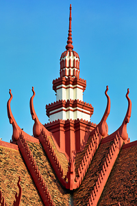 Ornate red and white temple roof and spire against blue sky. by Marco Brivio