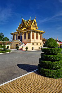 Golden roofed Cambodian building manicured bush and blue sky.