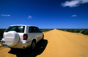 A white SUV on a long straight outback road.