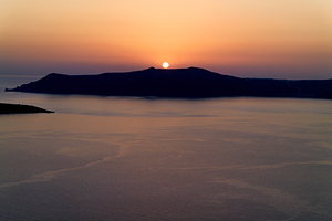 Golden sunset behind dark island calm ocean.