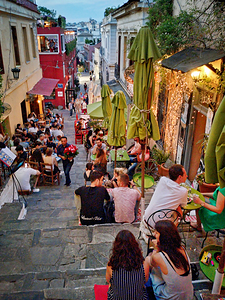 People enjoy drinks and food on a busy street in a city