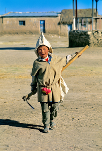 Indigenous boy with tools walks through a dusty village.