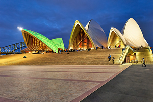 Sydney Opera House illuminated at dusk with people on steps.