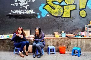 People eat food on small chairs in Hanoi Vietnam by Marco Brivio