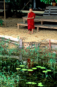 Young monk stands by water in Myanmar during daytime by Marco Brivio