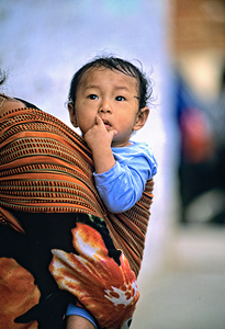 Curious child carried in a patterned fabric sling.