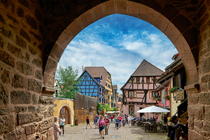 Visitors explore Riquewihr with timber framed houses under blue 
