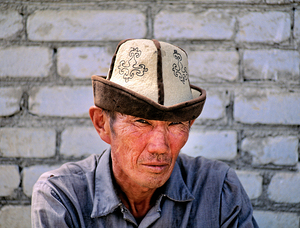 Man in traditional hat sits against a brick wall in Bukhara