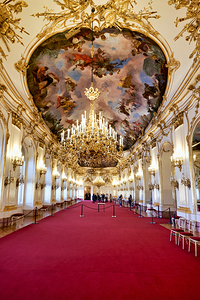 Ornate palace hall with chandeliers painted ceiling and red ca