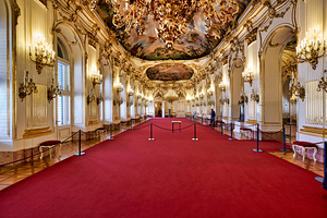 Stunning gilded palace hall with red carpet and chandeliers.
