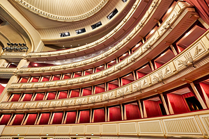 Ornate opera house interior with tiered red and gold balconies.