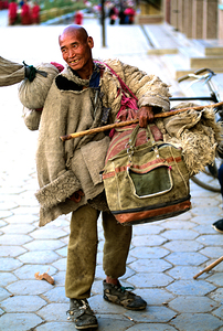Smiling man carries bundles while walking on street in Tibet