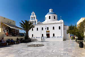 White Greek church with blue dome in sunny town square.