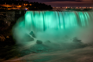Niagara Falls illuminated green at night with spectators.