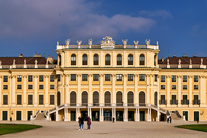 Ornate yellow palace facade with people and blue sky.