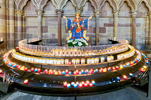 Visitors light votive candles near statue in Strasbourg Cathedra