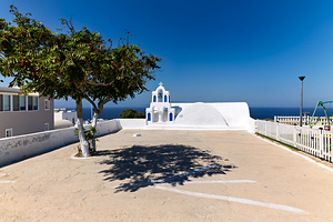 Iconic white church green tree and blue sea in Greece.