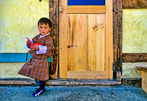 Bhutanese child in traditional dress holding a bowl and spoon.