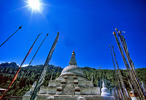 Buddhist stupa and prayer flags against a bright blue sky.