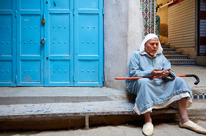 Portrait of a beggar sitting by a blue door in Fez Morocco