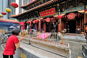 Woman prays with incense at colorful Chinese temple in Hong Kong by Marco Brivio