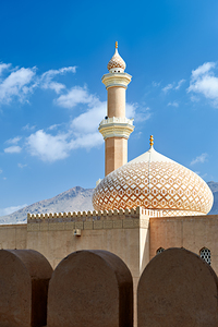 Nizwa Fort shows mosque and tower with blue sky and clouds