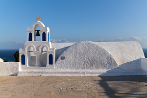 White Greek church with bell tower overlooking the sea.