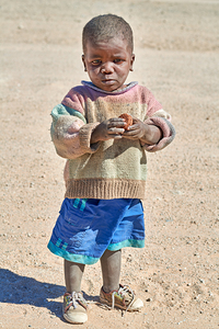 Sad child stands in Damaraland village in Namibia with a snack