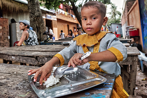 Child in traditional dress eating rice outdoors.