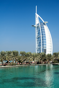 Burj Al Arab hotel stands tall by the water with palm trees