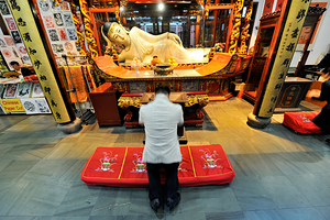 Worshipper kneels before Buddha statue in Shanghai temple