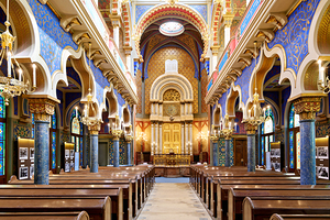 Grand ornate synagogue interior featuring golden ark and pews.