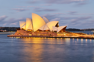 Sydney Opera House illuminated at dusk with harbor reflections.