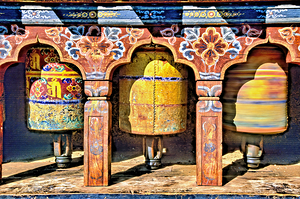 Ornate colorful Buddhist prayer wheels one spinning.