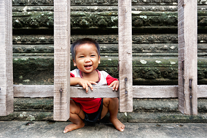 Joyful child peeking through wooden fence ancient background.