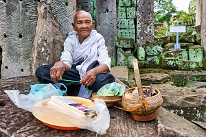Elderly person selling goods at ancient temple ruins.
