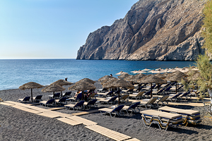 Sunny black sand beach with umbrellas loungers and rocky cliff