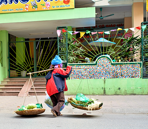 Woman carries baskets on busy street in Hanoi during daytime by Marco Brivio