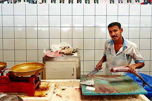 Man cuts fish at a market stall in Dubai during daylight hours