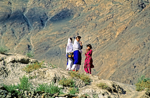 Women walk on hillside in Pakistan with mountains in view