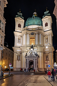 Illuminated baroque church at night with people on a wet street.
