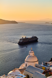 Cruise ship sails past Santorini dome at sunset.