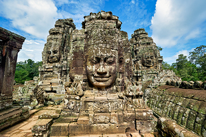 Ancient stone faces on Bayon Temple under a blue sky.
