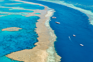 Aerial view of coral reefs and boats in turquoise ocean.