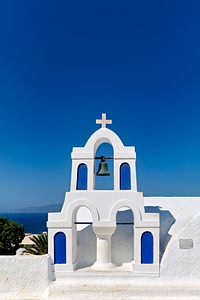 White bell tower against blue sky and sea.