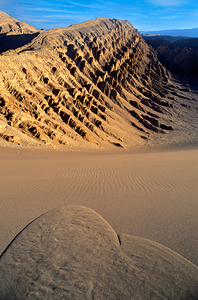 Eroded desert mountains and rippled sand under blue sky.